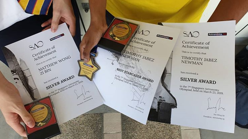 A close-up of multiple certificates and a star-shaped award laid out on a surface, including what appear to be gold and silver award certificates from an astronomy competition.